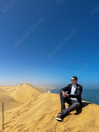 A young man sitting at sandy dunes on the seashore. Sandwich Harbour in Namibia