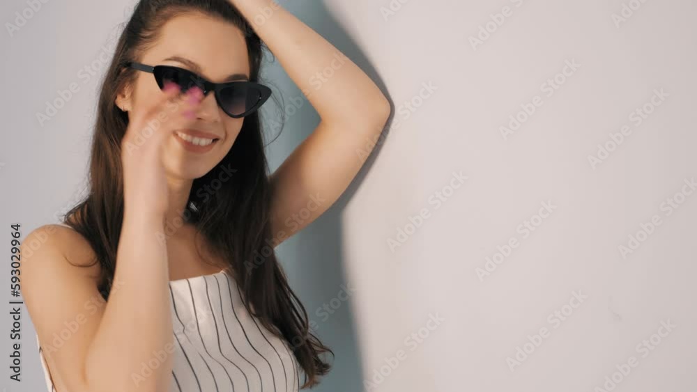 Portrait of young beautiful smiling female in trendy summer hipster overalls clothes. Sexy carefree woman posing near wall in studio. Positive model having fun indoors. In sunglasses