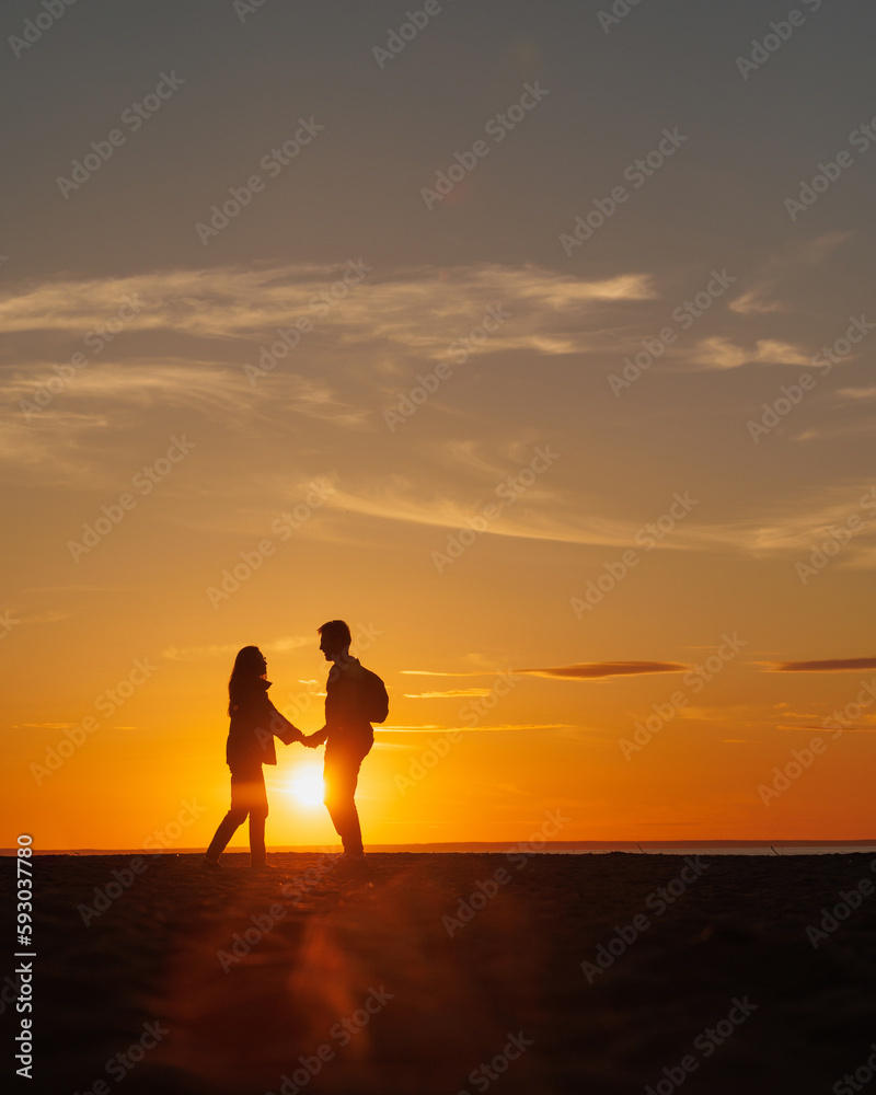 silhouette of a couple at sunset, woman and man walking along seashore in rays of sunset sunlight. walk and hug. place for text, romantic relationships, freedom and carelessness