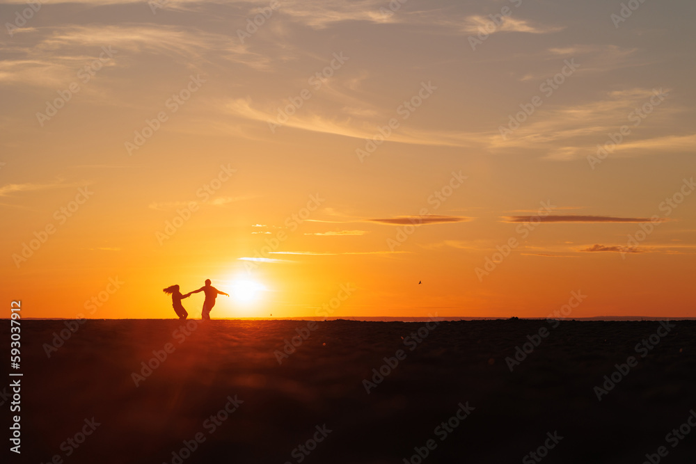 Obraz premium silhouettes of couple at sunset against bright sun sky. man and woman have fun in nature, walking and relaxing, relationships and falling in love. poster postcard romantic meetings against background 