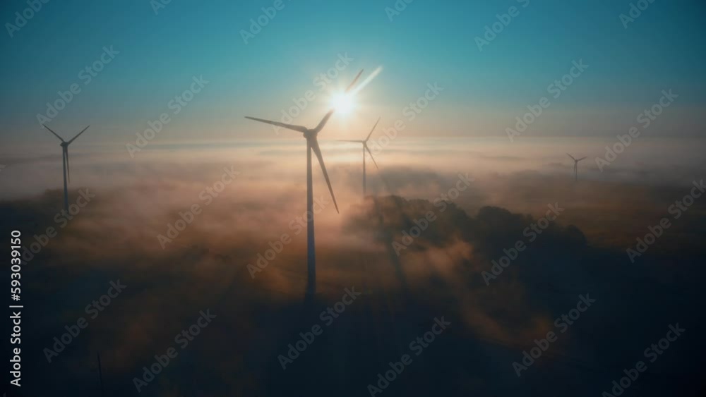 Wind farm at sunrise in heavy fog. Wind turbines generating green energy - concept of renewable electricity, sustainable energy, green power production