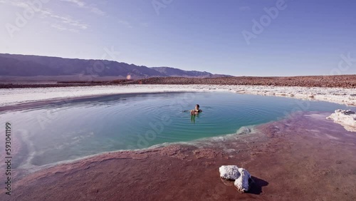 Woman floating alone in turquoise Baltinache salt pools in Atacama desert, Chile. Static shot in slow motion