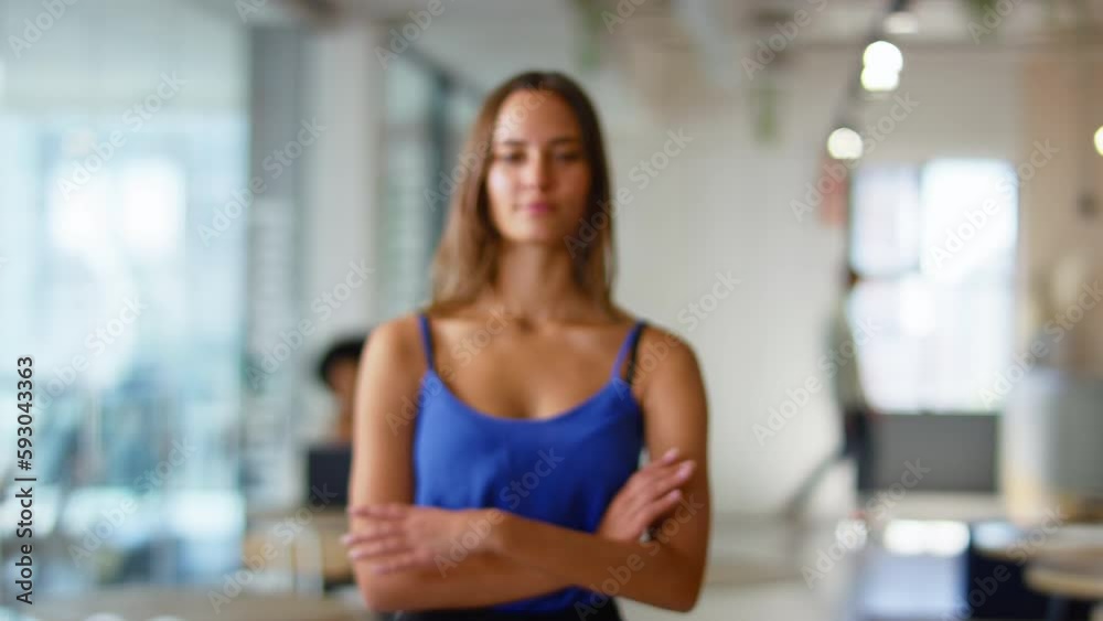 Camera tracks across serious young businesswoman walking into focus in modern open plan office looking into camera - shot in slow motion Camera tracks across serious young businesswoman walking into focus in modern open plan office looking into camera - shot in slow motion