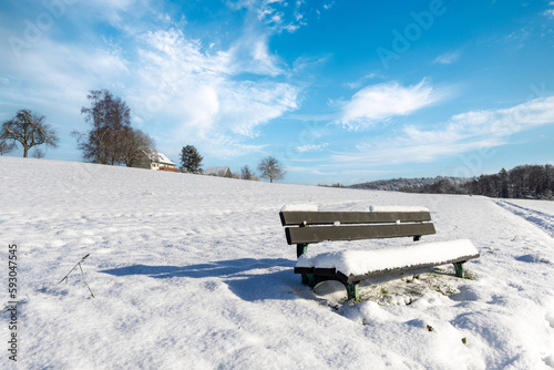 Empty bench covered in snow in a field on a clear winter sunny day