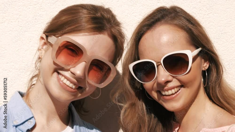 Two young beautiful smiling hipster female in trendy summer clothes and dress.carefree women posing in the street near white wall. Positive pure models having fun Two young beautiful smiling hipster female in trendy summer clothes and dress.carefree women posing in the street near white wall. Positive pure models having fun