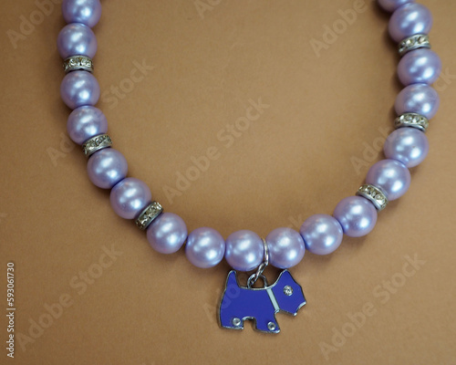 close elegant necklace for dogs made of purple beads and pendants in the shape of a purple dog with rhinestones lies on a broun background. view from above . dog accessories