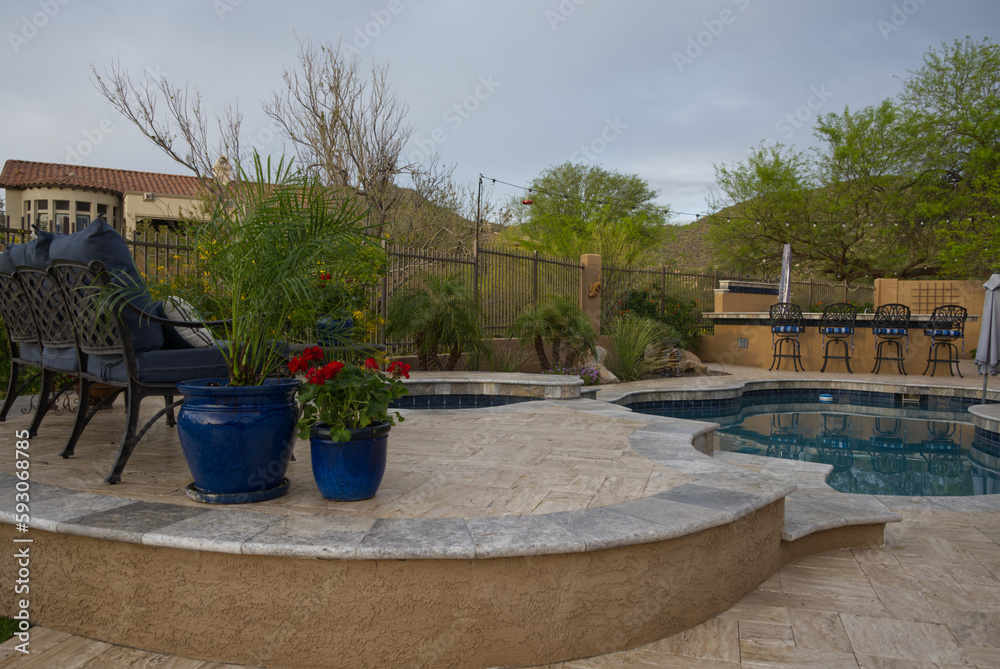 Fototapeta premium A desert landscaped backyard in Arizona featuring a travertine tiled pool deck, spa and outdoor kitchen.