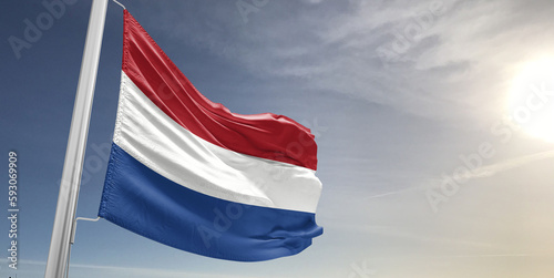 Netherlands national flag cloth fabric waving on beautiful sky grey Background.