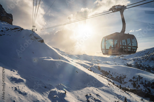 Gondola lift moving on cable over majestic snow covered Bernese mountains with cloudy sky and bright sun in background at Jungfrau, Switzerland, winter holiday and nature concept
