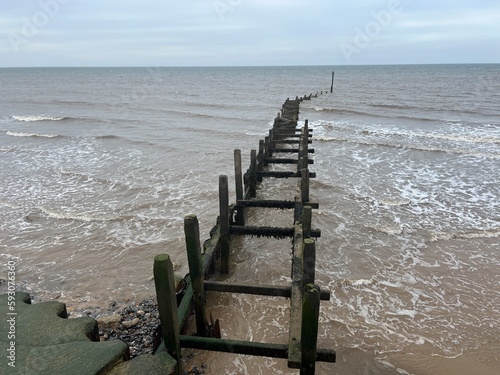 Wooden breakwater on the shore of the sandy beautiful beach at Overstrand Norfolk East Anglia scenic view out to horizon across ocean in cloudy weather. photo