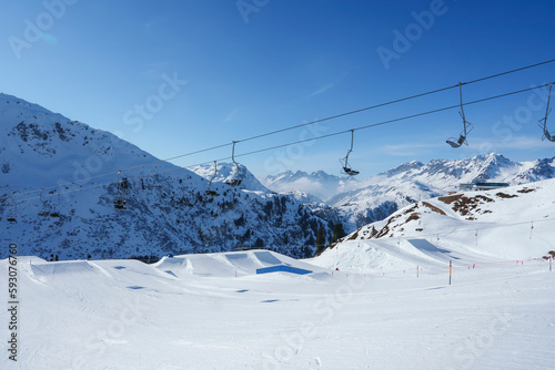 Ski lifts over snow covered land with mountains in background during sunny day, winter holiday travel concept © Aerial Film Studio