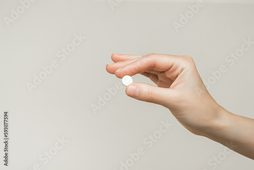 female hand holding a round white pill on a gray background