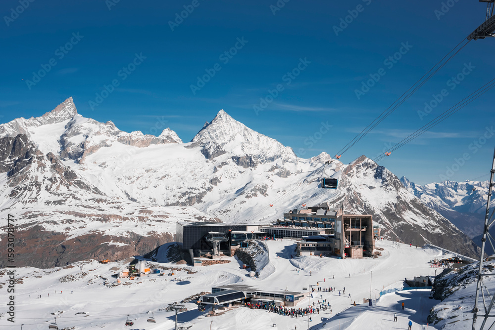 Ski chairlift passing over snow covered landscape and leading towards majestic matterhorn mountain range at resort under blue sky at Zermatt, Switzerland, winter holiday travel concept