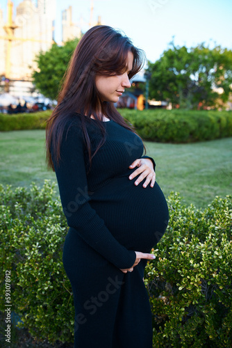 pregnant girl holding her belly, around flowers and plants, in garden