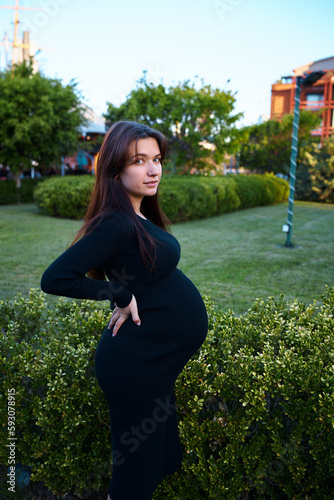 pregnant girl holding her belly, around flowers and plants, in garden