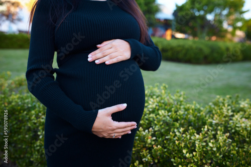pregnant girl holding her belly, around flowers and plants, in garden