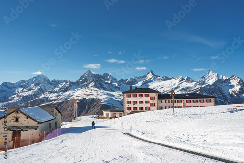Exterior of luxurious hotel building and beautiful view of snowcapped mountain range with blue sky in background during sunny day at Zermatt, Switzerland, winter holiday travel concept