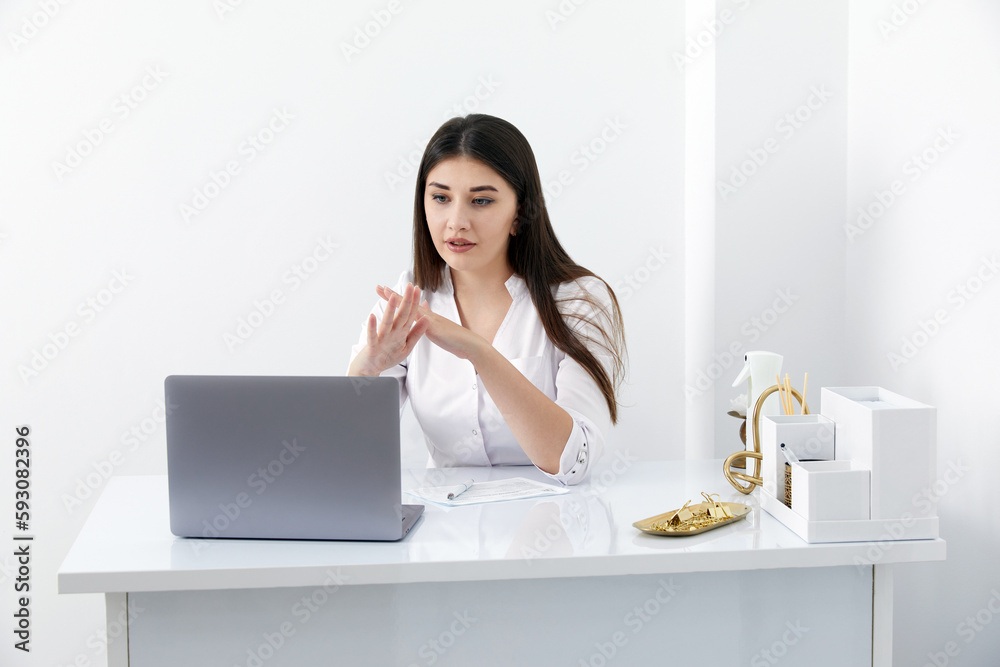 Portrait of female doctor talking to online patient on laptop screen sitting at clinic office desk giving online consultation for domestic health treatment Portrait of female doctor talking to online patient on laptop screen sitting at clinic office desk giving online consultation for domestic health treatment