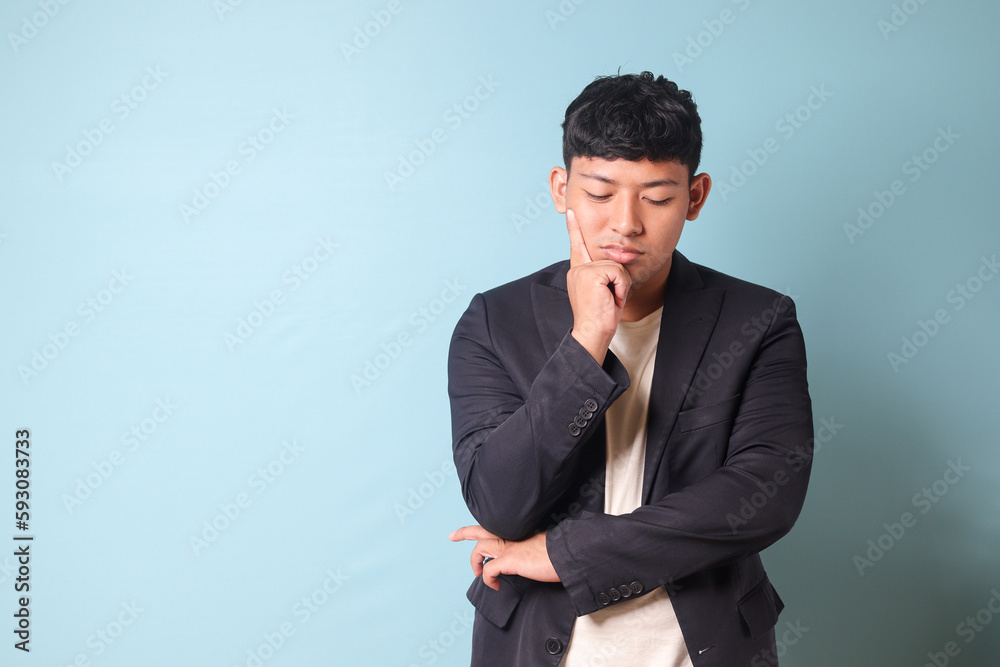 Portrait of young Asian business man in casual suit closing eyes thingking hard. Isolated image on blue background Portrait of young Asian business man in casual suit closing eyes thingking hard. Isolated image on blue background