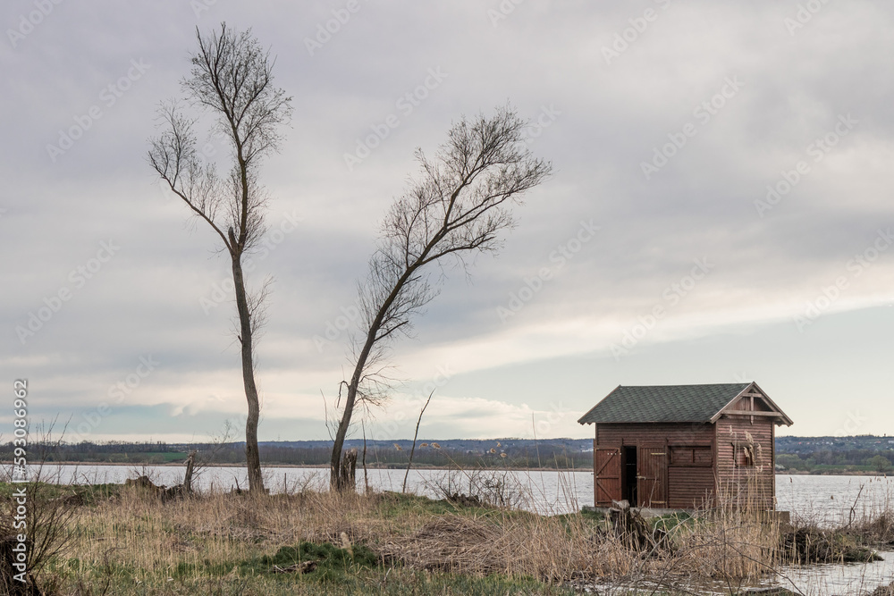 Small wooden fishing house next to a lake, cloudy spring day Small wooden fishing house next to a lake, cloudy spring day