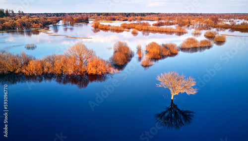 Spring flood rural landscape. Trees, meadow, bushes, fields, country road under High Water inundation. Sky, clouds reflection in evening light. Freshet Overflow aerial view. Floodplain area.