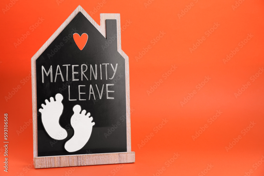 Wooden house figure with words Maternity Leave and paper cutout of baby feet on orange background. Space for text Wooden house figure with words Maternity Leave and paper cutout of baby feet on orange background. Space for text