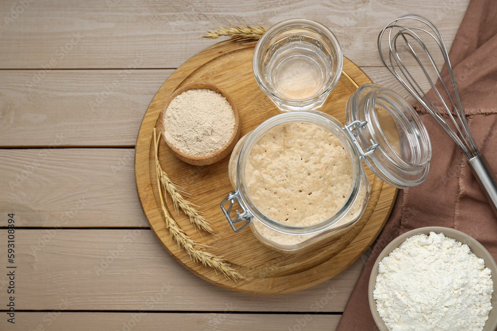 Leaven, ears of wheat, whisk, water and flour on beige wooden table, flat lay Leaven, ears of wheat, whisk, water and flour on beige wooden table, flat lay