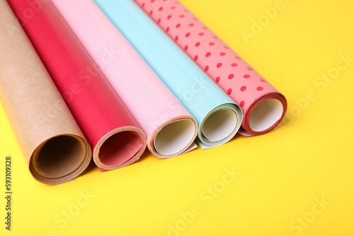 Rolls of colorful wrapping papers on yellow background, closeup