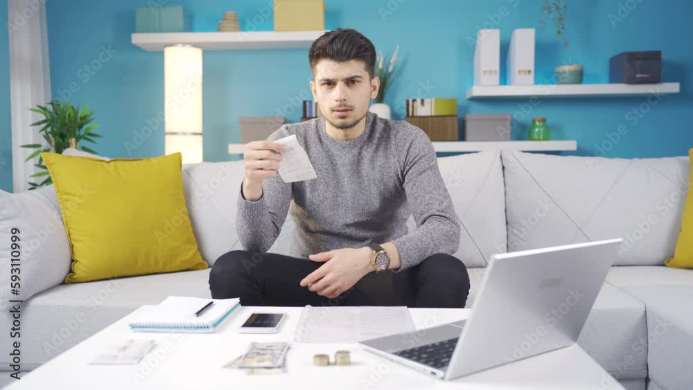 The young man plans the budget and is disappointed. Young man sitting on sofa and reading bank cards and calculating online loan debt payments. The young man plans the budget and is disappointed. Young man sitting on sofa and reading bank cards and calculating online loan debt payments.