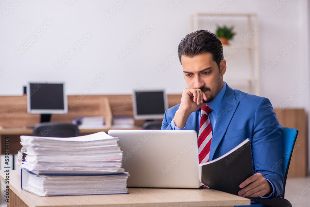 Young male employee unhappy with excessive work at workplace Young male employee unhappy with excessive work at workplace