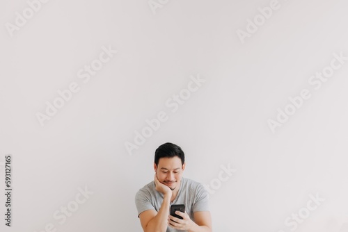 Minimal portrait of Asian man using smartphone at the bottom with empty space.