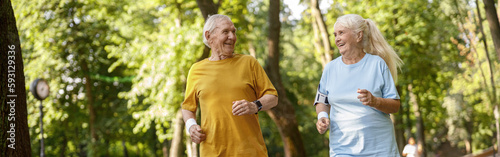 Positive senior family couple run tgether along road in park