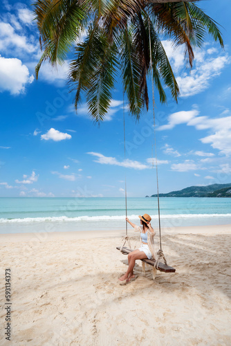 Young woman traveler enjoying on the swing at beautiful tropical white sand beach, Summer vacation and Travel concept