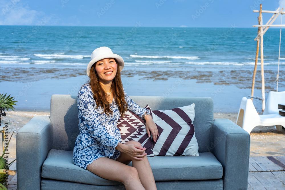 Beautiful Asian woman summer vacation sitting on sofa with pillows on the beach in front of island resort