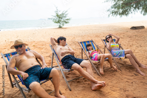 Group of Happy Multi-Generation Asian family in swimwear enjoy and fun outdoor lifestyle resting on beach chair together at tropical island beach during travel ocean on summer holiday vacation.