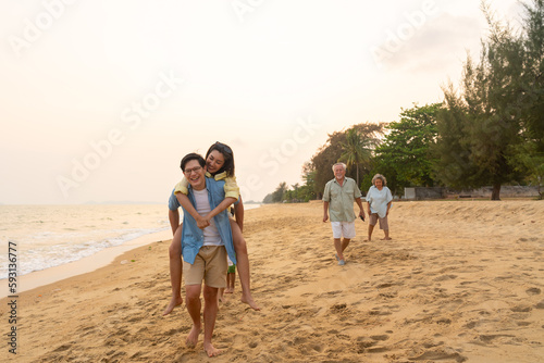 Happy Asian family Asian couple enjoy and fun outdoor lifestyle travel tropical island beach on holiday vacation. Wife piggyback ride her husband walking on the beach at summer sunset.
