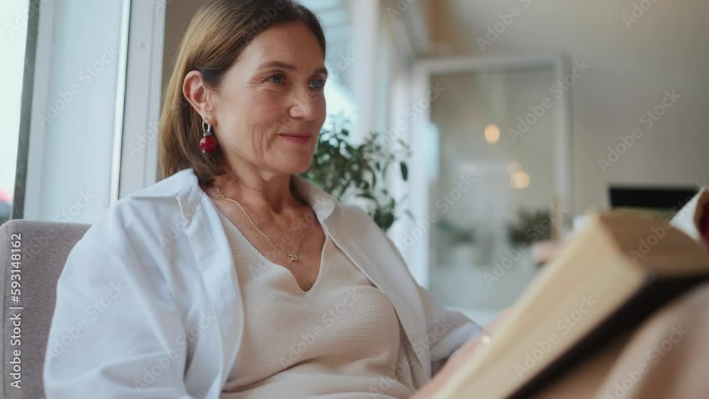 Cute elderly woman in white shirt looking at window and reading book in cafe Cute elderly woman in white shirt looking at window and reading book in cafe