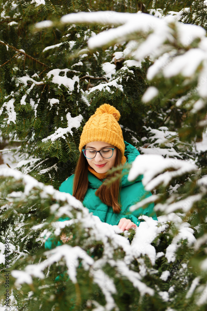 woman in yellow hat, glasses and green jacket walks in park in winter