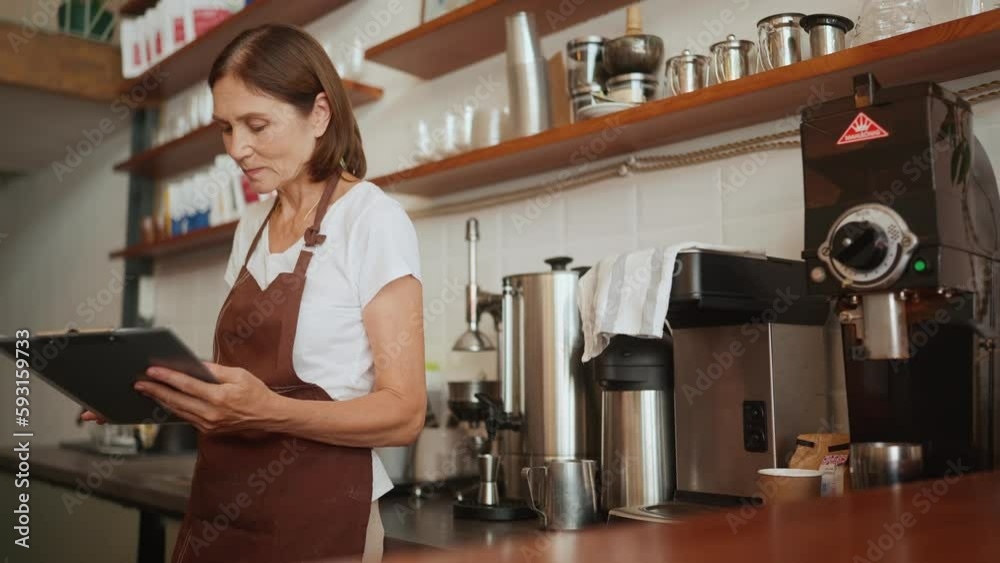 Serious aged woman barista signs paper documents behind counter in cafe Serious aged woman barista signs paper documents behind counter in cafe