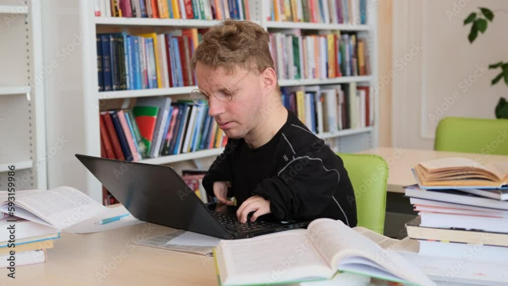 a man with disabilities works at a laptop in the library. a man with disabilities works at a laptop in the library.