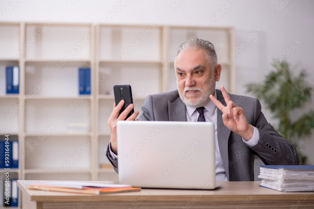 Old male employee speaking by phone at workplace Old male employee speaking by phone at workplace