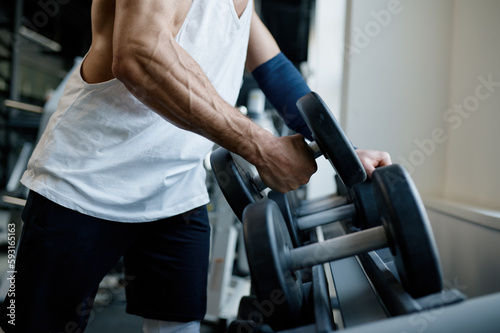 Sportsman with athletic body taking dumbbells to do exercise with weights