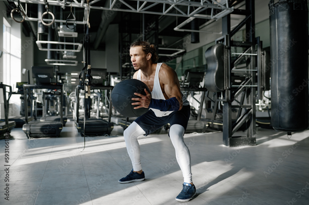 Athletic sportsman in sportswear doing squats with medicine balls at gym Athletic sportsman in sportswear doing squats with medicine balls at gym