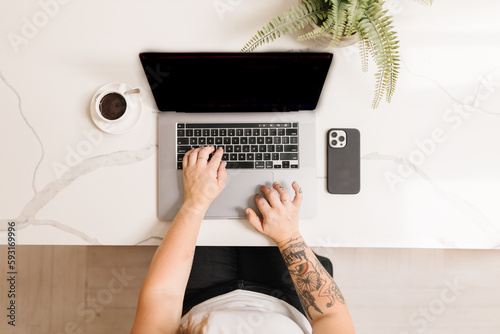 Tattooed arms typing on a computer with espresso and phone