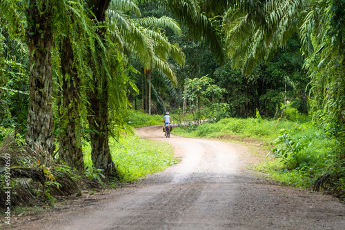 Bikepacking woman cycling on dirt road surrounded by thai jungle photo
