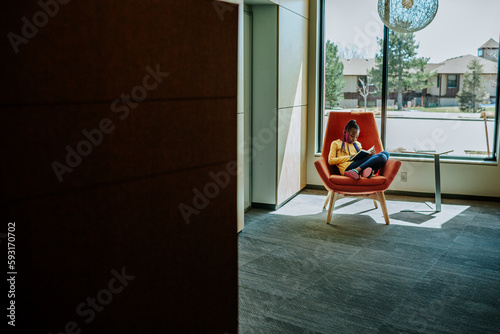 pull back of young black girl reading in front of a window