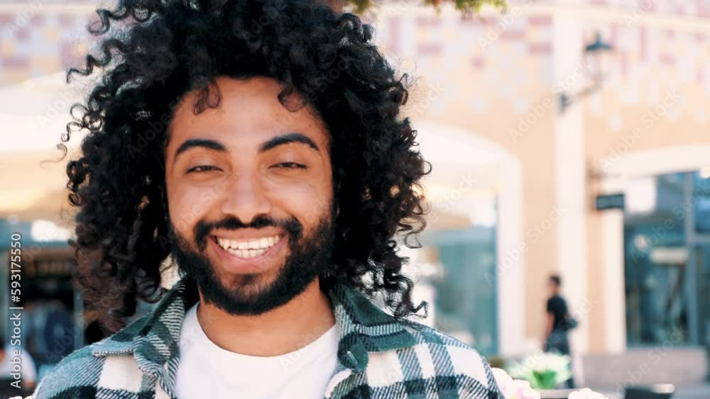 Handsome smiling hipster model. Sexy unshaven Arabian man dressed in summer clothes. Fashion male with long curly hairstyle posing in the street at sunset. Cheerful and happy Handsome smiling hipster model. Sexy unshaven Arabian man dressed in summer clothes. Fashion male with long curly hairstyle posing in the street at sunset. Cheerful and happy