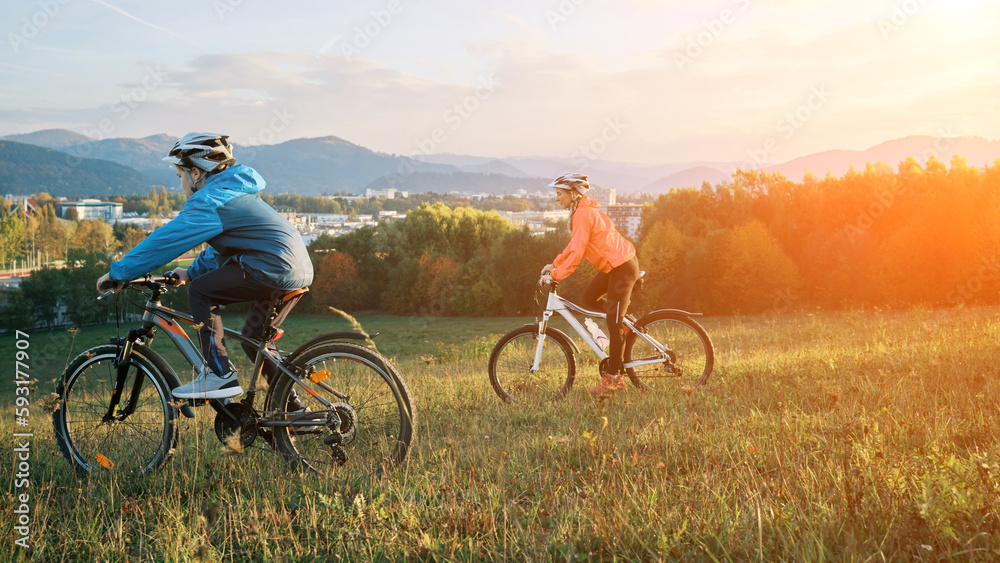 Obraz premium Mother and son ride a bike. Happy cute boy in helmet learn to riding a bike in park on green meadow in autumn day at sunset time. Family weekend. 