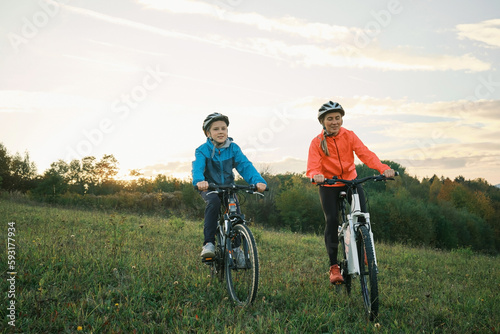 Mother and son ride a bike. Happy cute boy in helmet learn to riding a bike in park on green meadow in autumn day at sunset time. Family weekend. 