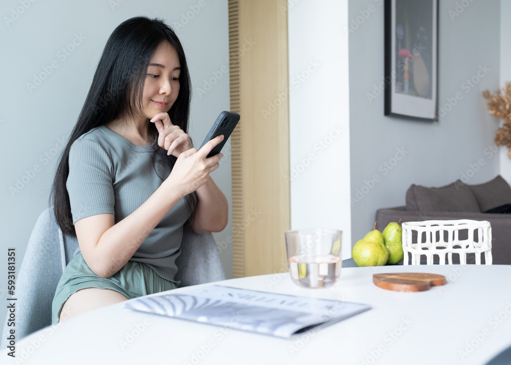 Smiling Chinese woman using mobile phone app, online shopping, thinking, deciding, video call, using laptop, working casually at home. Girl at home checking social media, holding smartphone. Smiling Chinese woman using mobile phone app, online shopping, thinking, deciding, video call, using laptop, working casually at home. Girl at home checking social media, holding smartphone.